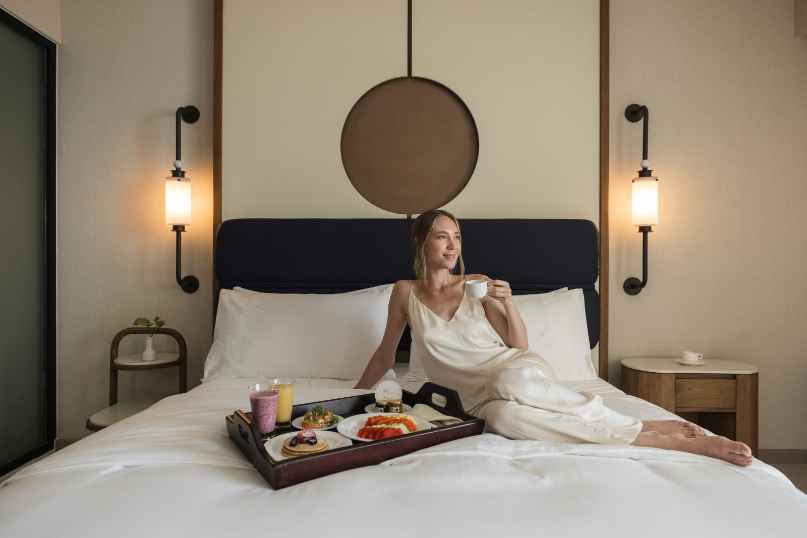 una mujer sentada en una cama con una bandeja de comida