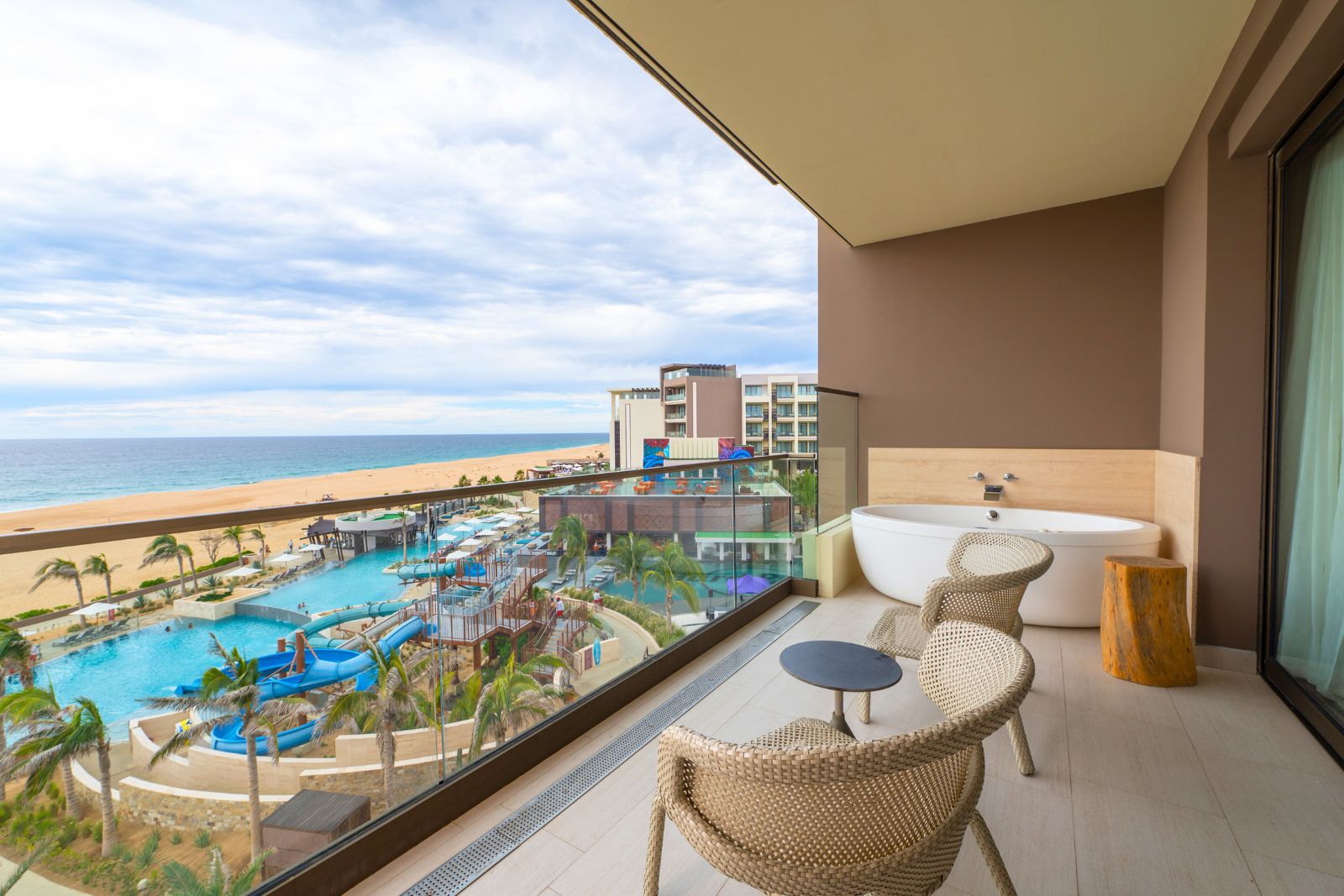 a balcony with a tub and chairs overlooking a beach